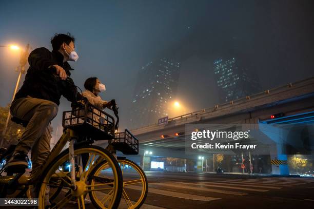 Couple wear protective masks to protect against the spread of COVID-19 as they stop on their shared bikes to look up at the CCTV building obscured by...