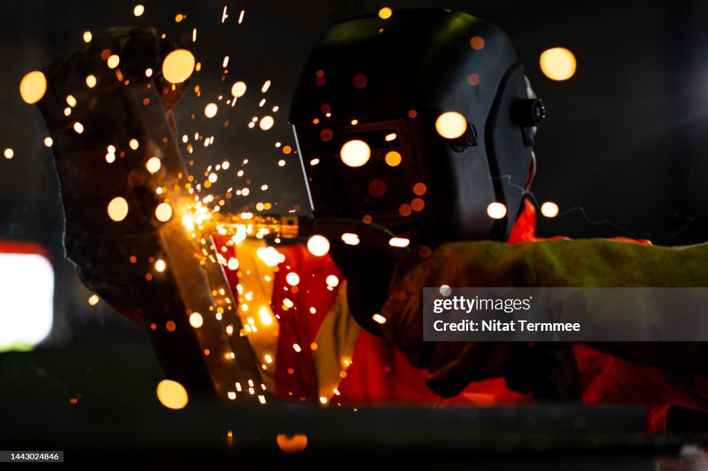 Safety First in Welding Operations. An African American Industrial welder working welding metal seams of a construction beam in a metal plant wearing a protective mask to protect sparks on a metal work welding.