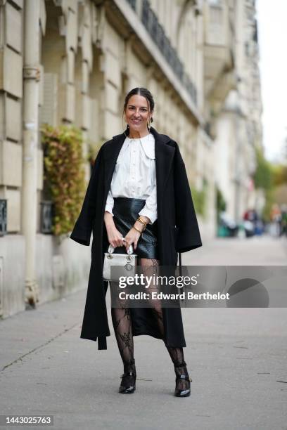 Alba Garavito Torre wears gold large with white pendant earrings, a white blouse with big from Peter Pan collar and lantern sleeves, a black long...