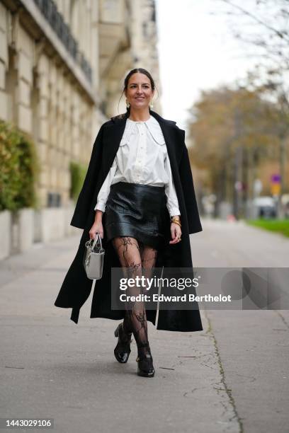 Alba Garavito Torre wears gold large with white pendant earrings, a white blouse with big from Peter Pan collar and lantern sleeves, a black long...