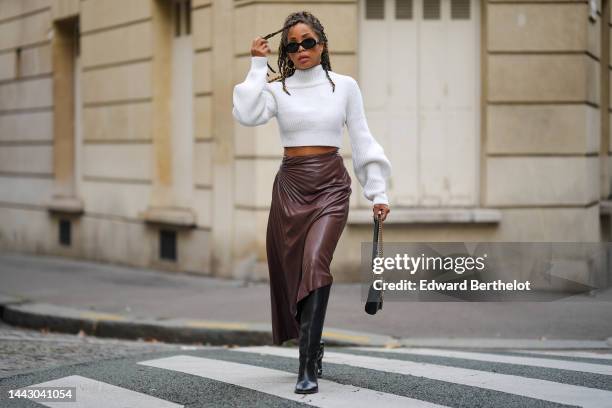 Ellie Delphine wears black sunglasses from Celine, gold earrings, a white ribbed wool high neck / puffy long sleeves / cropped top, a black shiny...