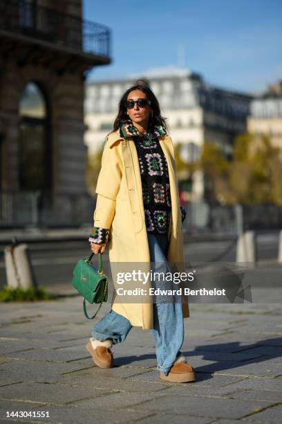 Gabriella Berdugo wears black sunglasses from Versace, gold earrings, a black / brown / green / purple / white print pattern puffy wool / zipper...