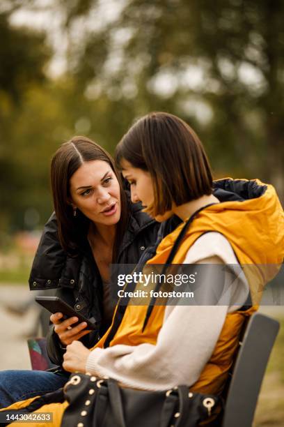 two girlfriends sitting on the street bench, looking at social media posts via smart phone, chatting and bonding - meme text stock pictures, royalty-free photos & images