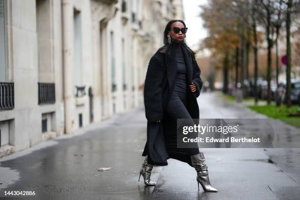 Emilie Joseph wears black sunglasses, a silver and rhinestones fringed pendant earrings, a black turtleneck / long sleeves / backless / long tube...