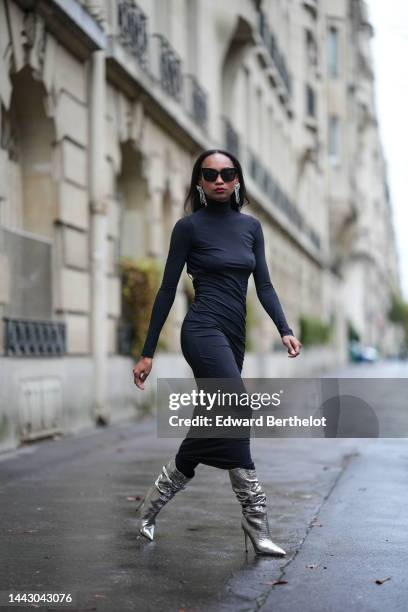 Emilie Joseph wears black sunglasses, a silver and rhinestones fringed pendant earrings, a black turtleneck / long sleeves / backless / long tube...