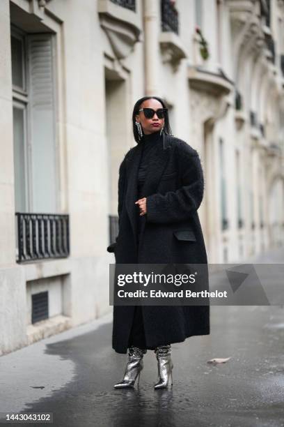 Emilie Joseph wears black sunglasses, a silver and rhinestones fringed pendant earrings, a black turtleneck / long sleeves / backless / long tube...