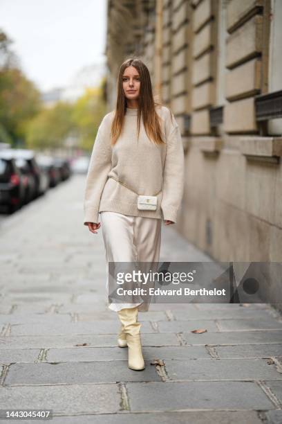 Diane Batoukina wears a beige wool pullover, a white shiny leather belt bag from Chanel, white latte silk midi skirt, pale yellow shiny leather heels...