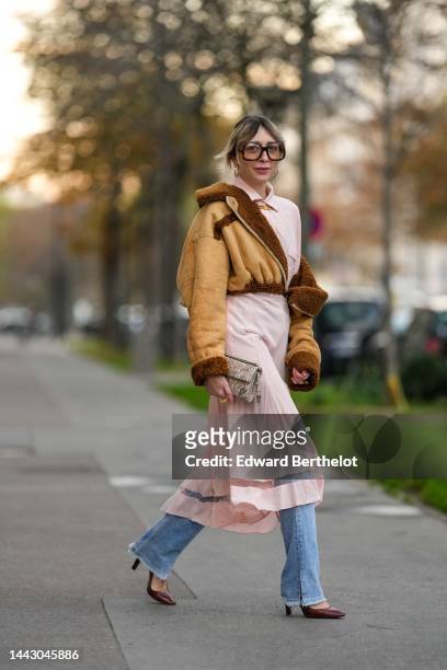 Emy Venturini wears black square sunglasses from Gucci, gold earrings, a gold large chain necklace, a pale pink long shirt midi dress from Fendi, a...