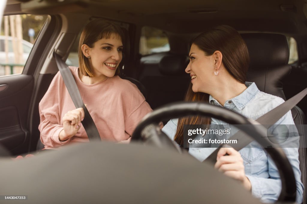 Young woman and her frined sitting in front in a car and putting their seat belts on before going for a ride