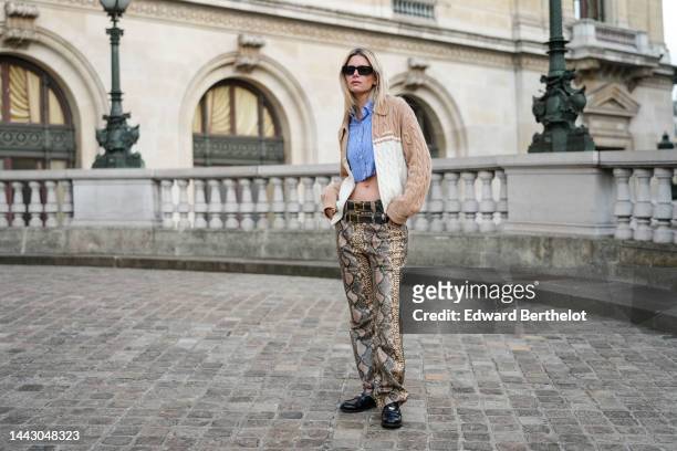 Natalia Verza wears black square sunglasses from Prada, gold earrings, a pale blue striped print pattern cropped shirt from Miu Miu, a beige and...