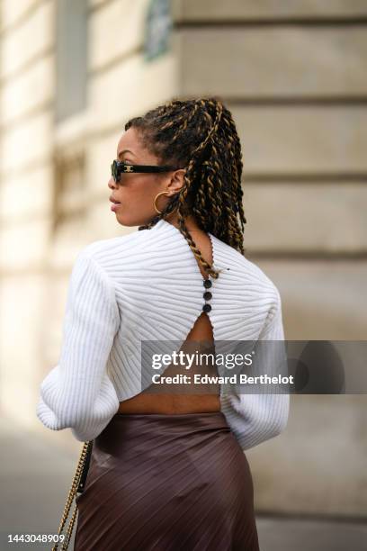 Ellie Delphine wears black sunglasses from Celine, gold earrings, a white ribbed wool high neck / puffy long sleeves / cropped / backless pullover, a...