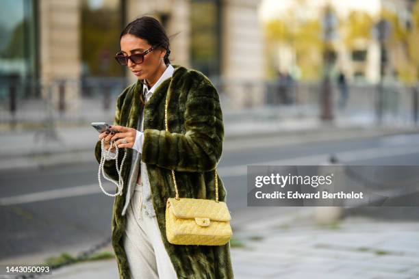 Gabriella Berdugo wears brown sunglasses, gold and silver earrings, silver and gold large long necklace, a white cropped shirt, a pale gray wool...