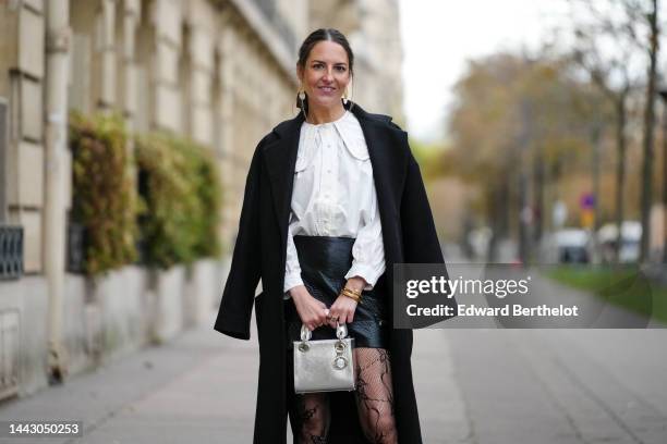 Alba Garavito Torre wears gold large with white pendant earrings, a white blouse with big from Peter Pan collar and lantern sleeves, a black long...