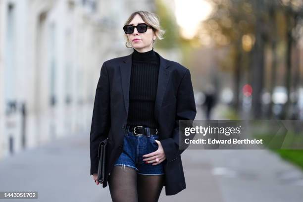 Emy Venturini wears black sunglasses from Voodoo, gold large earrings from YSL / Saint Laurent Paris, a black braided wool turtleneck pullover from...