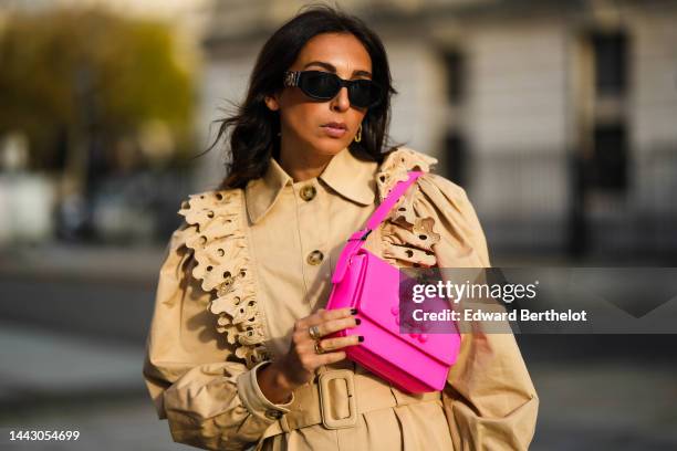 Gabriella Berdugo wears black sunglasses from Versace, a beige with embroidered ruffled shoulder / long puffy sleeves / belted / midi coat from...