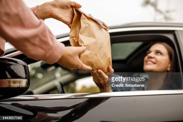 junge frau lächelt serviceperson bei der durchfahrt an, während sie ihre bestellung zum mitnehmen entgegennimmt - drive through stock-fotos und bilder