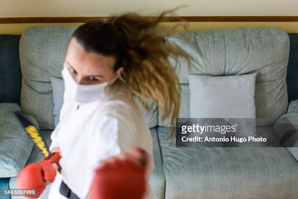 blonde girl in a mask practicing karate at home.giving a punch and doing a kata. black karate belt and red gloves. quarantine virus. home isolated. - karate girl isolated stock pictures, royalty-free photos & images