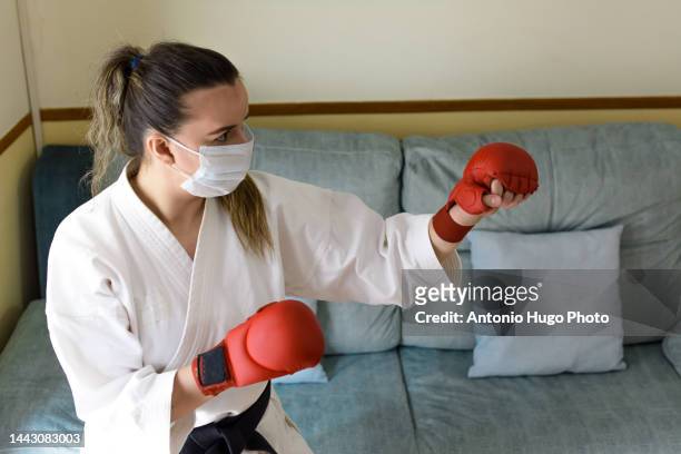 blonde girl in a mask practicing karate at home.giving a punch and doing a kata. black karate belt and red gloves. quarantine virus. home isolated. - karate girl isolated stock pictures, royalty-free photos & images