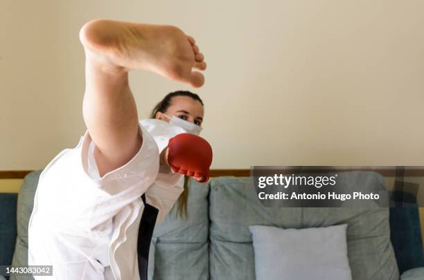 blonde girl in a mask practicing karate at home. doing a flying kick. black karate belt and red gloves. quarantine virus. home isolated. - karate girl isolated stock pictures, royalty-free photos & images