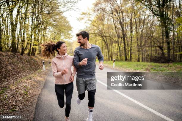 glückliches sportliches paar, das spaß beim laufen am frühlingstag hat - couple running stock-fotos und bilder