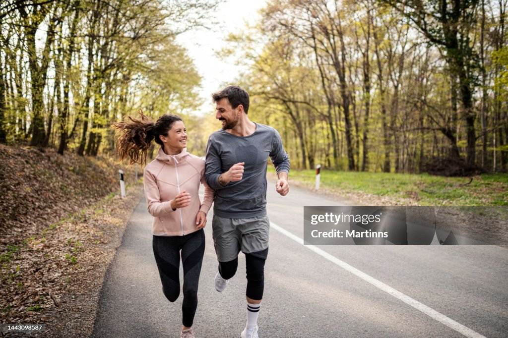 Feliz pareja atlética divirtiéndose mientras corre en el día de primavera