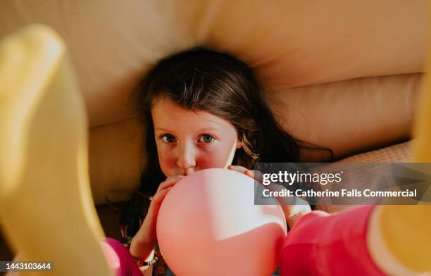 a cute little girl blows up a pink balloon - blowing up balloon stock-fotos und bilder