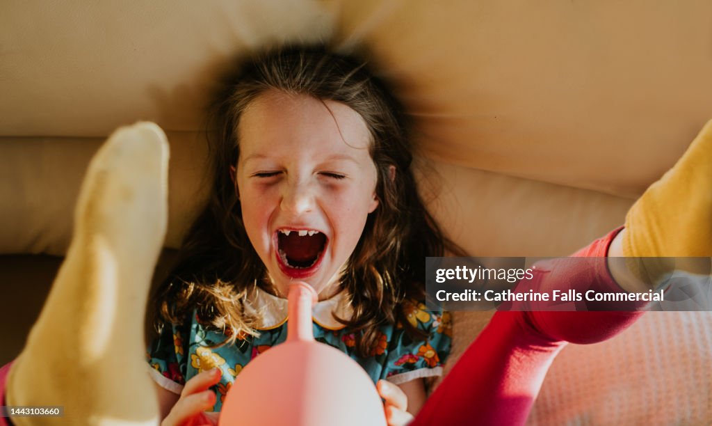Joyful image of a child letting go of a balloon, it deflates quickly making a noise and blowing her back