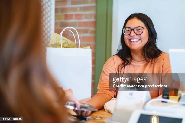 hispanic and white females in small town america boutique using credit cards and electronic devices payments on the go photo series - gift shop stock pictures, royalty-free photos & images
