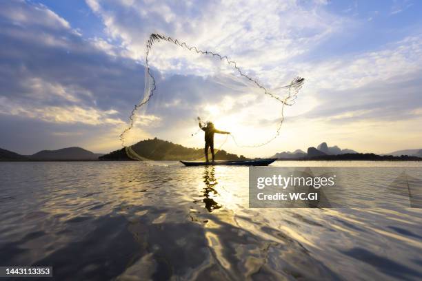 fisherman throwing fishing nets during sunset on boats - fishing net stockfoto's en -beelden