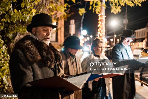 mature people singing christmas carols outdoors at night - carol singer stock pictures, royalty-free photos & images