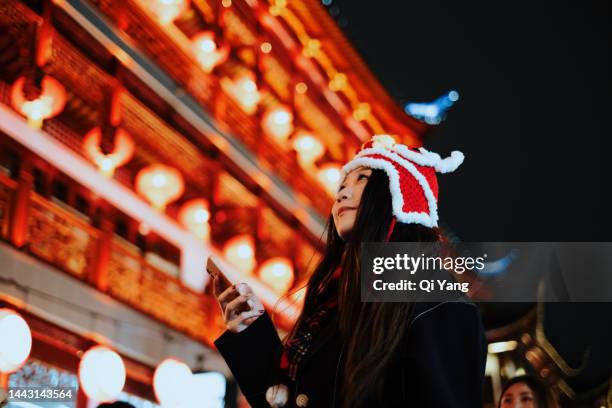 asian young woman celebrating chinese new year using smartphone on the street, shanghai, china - shanghai calling stock pictures, royalty-free photos & images