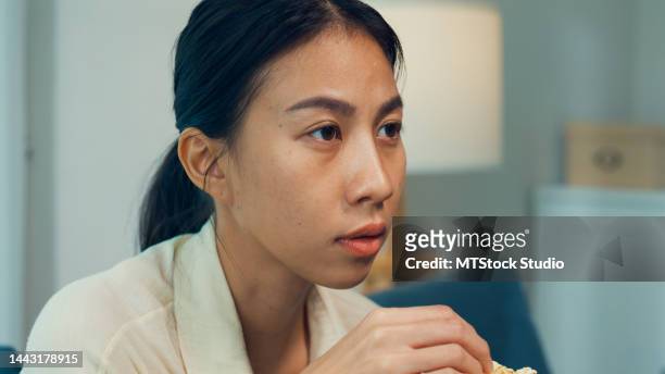 close-up young asian curious girl on sofa eat popcorn excited watch documentaries channel movie or mysteries show on television in streaming online vod, at home. - scandal television show stock pictures, royalty-free photos & images