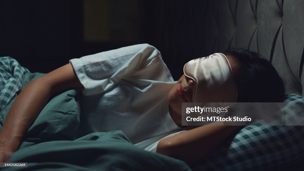 Young beautiful Asia girl lay on bed soft pillow wear eyes mask relaxing from work deep breath sleep tight and well on comfort bed in bedroom cozy home at night.