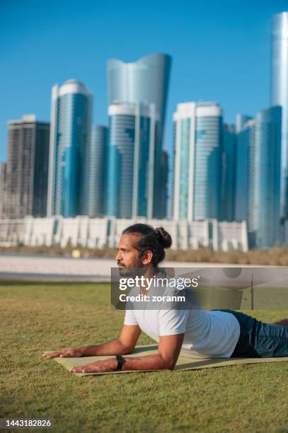 bearded man practicing yoga on the public park lawn in abu dhabi, assuming cobra pose - yoga office arab stock pictures, royalty-free photos & images