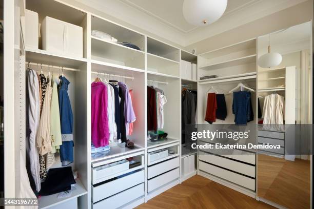 white wardrobe with clothes on hangers at home - closet stock pictures, royalty-free photos & images