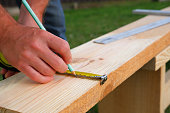 Male carpenter measuring wooden blank with the lines and making marks with a pencil and tape. Close up view.