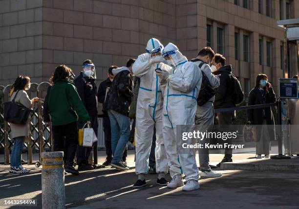 Security guards dressed in protective equipment to protect against the spread of COVID-19 look at a mobile phone as office workers wait to enter an...