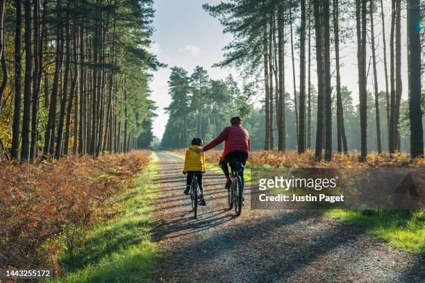 rear view of a young girl cycling in the forest with her father on a beautiful autumnal sunny day - child mental health wellness foto e immagini stock