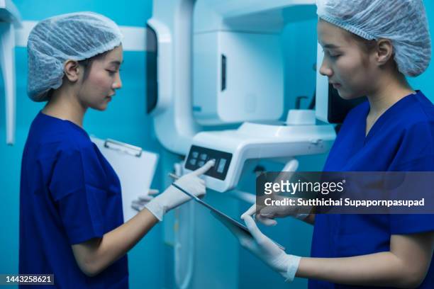 two asian female using digital tablet and discuss about the dental x-ray machine. - critical care stock-fotos und bilder