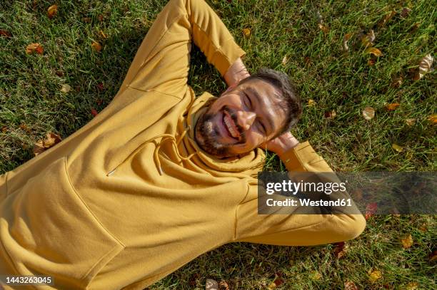 cheerful man in yellow hooded jacket lying on grass at park - hands behind head stock pictures, royalty-free photos & images