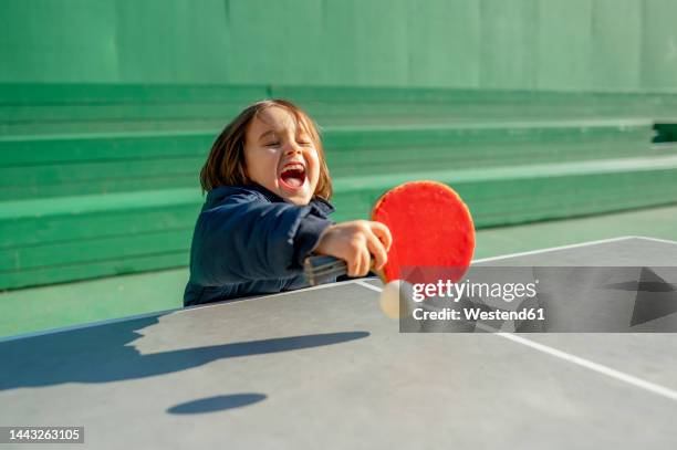 cheerful boy playing table tennis on sunny day - paddle tennis stock-fotos und bilder