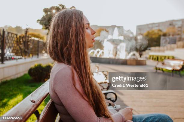 woman with long hair smoking electronic cigarette on bench - exhale stock pictures, royalty-free photos & images