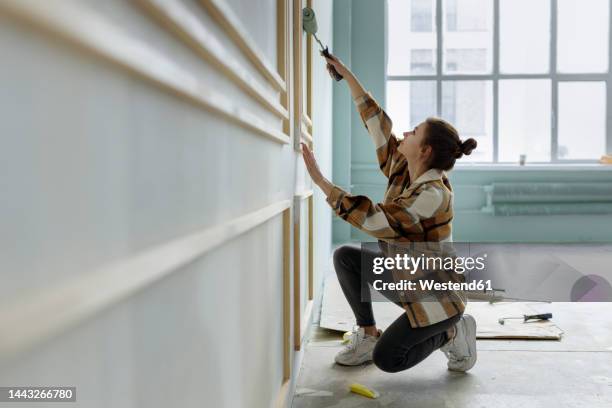 young woman applying paint on wall in apartment - renovation stock-fotos und bilder