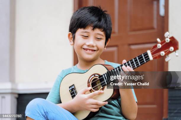 little boy playing ukulele - ukulele stock-fotos und bilder