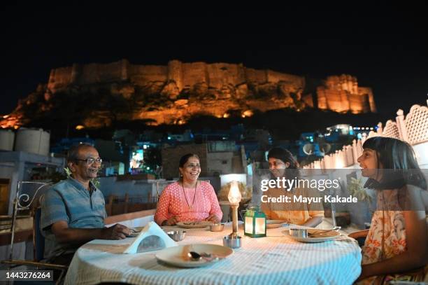 multi-generation family sitting at a roof top restaurant for dinner with the backdrop of meharangarh fort, jodhpur - family trip in laws stock pictures, royalty-free photos & images