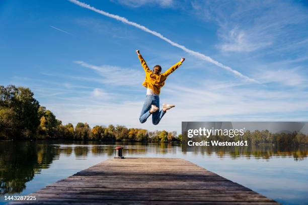 carefree woman jumping on jetty under vapor trail - happy jumping stock-fotos und bilder