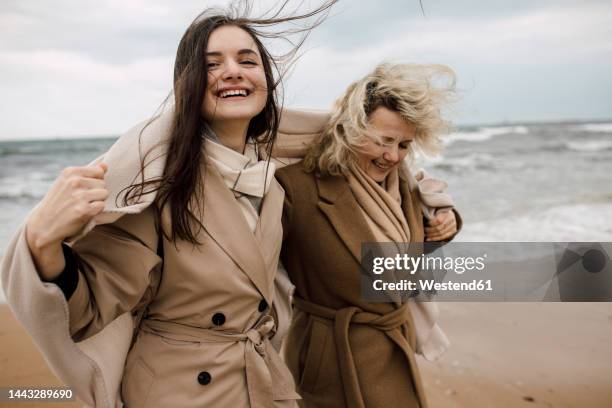 mother and daughter wearing overcoats enjoying at beach - オーバーコート ストックフォトと画像