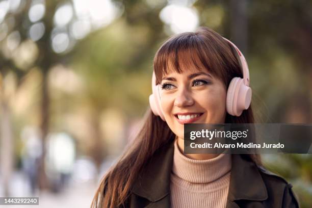 close-up frontal portrait of a young smiling caucasian woman while listening to music with wireless headphones. - portrait frontal stock pictures, royalty-free photos & images