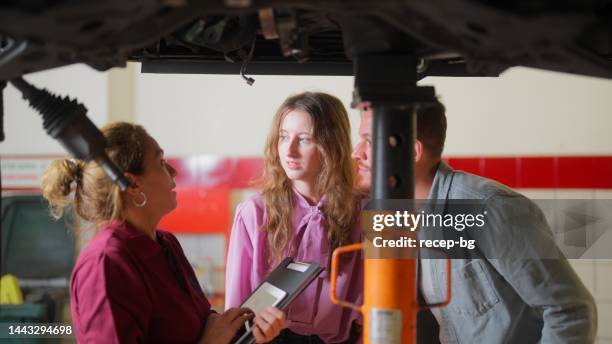 kfz-mechaniker-experte überprüft kaputtes auto und diskutiert mit paar - happy client by broken car stock-fotos und bilder