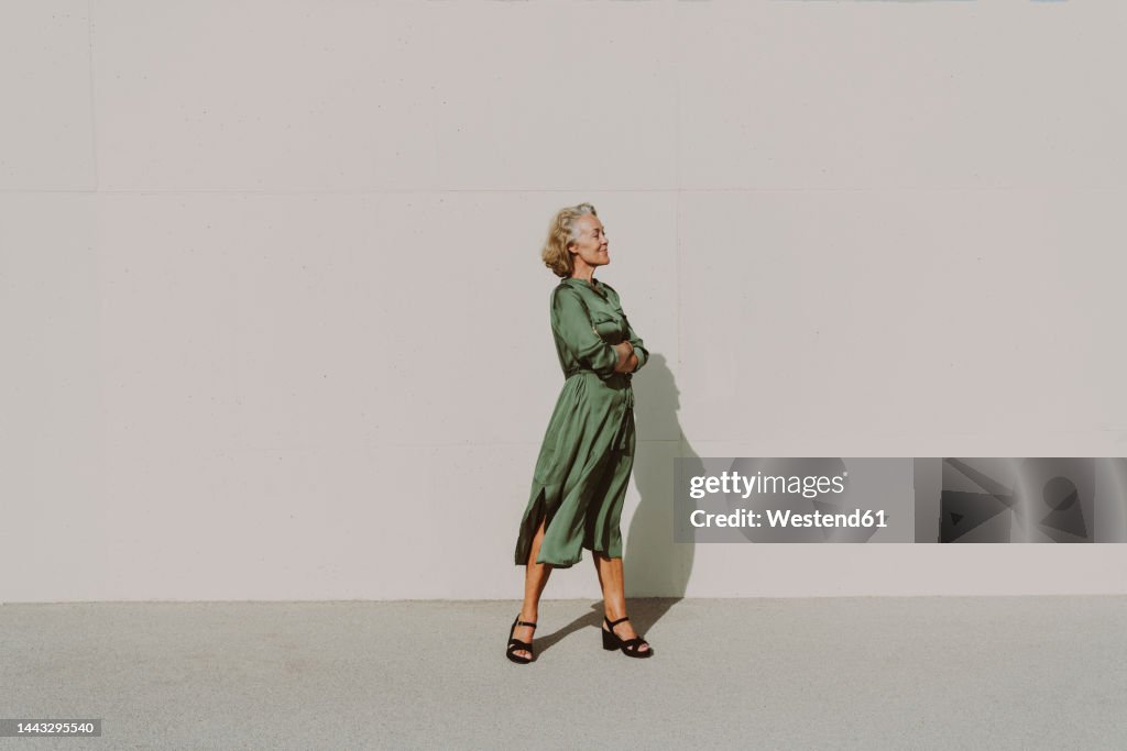 Thoughtful woman with arms crossed in front of white wall